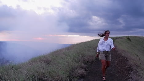 Woman-walks-on-volcano-rim-trail-buffeted-by-strong-summit-wind