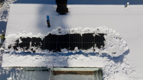 Aerial-view-above-partly-snow-covered-solar-panels-on-a-house-roof,-winter-day