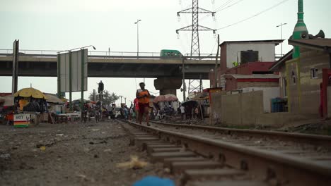 Zona-De-Tugurios-En-Accra,-Ghana,-Con-Vías-De-Tren-Y-Gente-Caminando-Vestida-Con-Telas-Tradicionales-De-Ghana