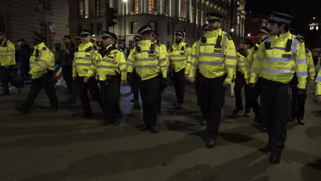 Metropolitan-police-officers-in-fluorescent-yellow-jackets-form-a-cordon-line-and-lead-the-front-of-a-protest-marching-on-a-road-during-a-public-order-incident-at-night
