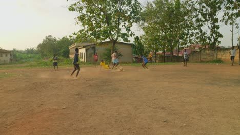 Junge-Männer-Spielen-Fußball-Auf-Einem-Gemeinschaftsfeld,-Während-Ein-Junge-Zu-Boden-Fällt,-Während-Ein-Anderer-Auf-Den-Torwart-Zuläuft,-Aber-Scheitert,-Gemeinschaftsfußballfeld,-Kumasi,-Ghana