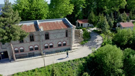 Drone-panning-from-left-to-right-following-length-of-the-entire-chapel-as-a-tourist-is-walking-by,-on-Krastova-Gora,-Rhodope-Mountain-in-Bulgaria