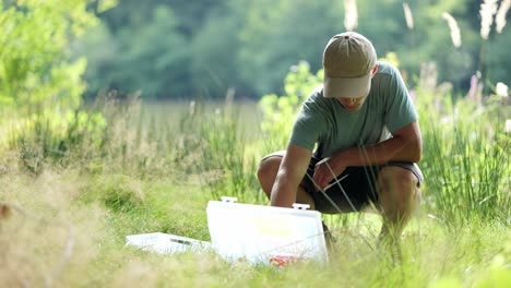 El-Joven-Pescador-Se-Sienta-En-La-Hierba-Alta-De-La-Pradera-Y-Prepara-Su-Equipo-Para-Pescar.