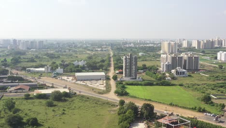RAJKOT-CITY-AERIAL-VIEW-PHONE-CAMERA-GOING-AHEAD-THERE-IS-A-TRP-GAME-ZONE,-AND-A-FIELD-BESIDES-A-LARGE-HIGH-RISE-BUILDING