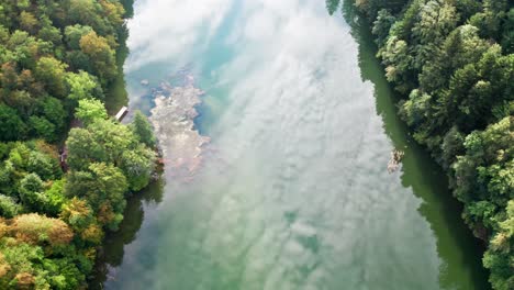 Reflecting-deep-green-blue-river-through-forest-with-different-colored-trees,-aerial-drone