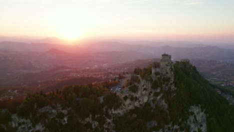 Three-towers-of-San-Marino,-Italy,-drone-pull-out-view-during-sunset