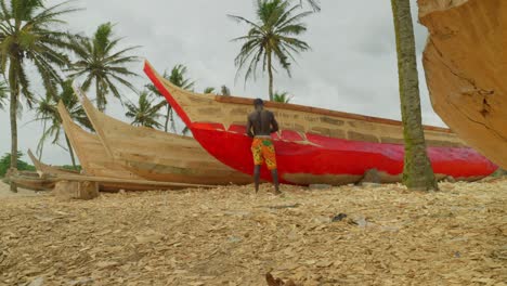 Establecido-De-Un-Hombre-Negro-Solitario-Pintando-Un-Barco-Tradicional-De-Pescador-De-Madera-Roja-En-Una-Playa-Tropical-De-Arena