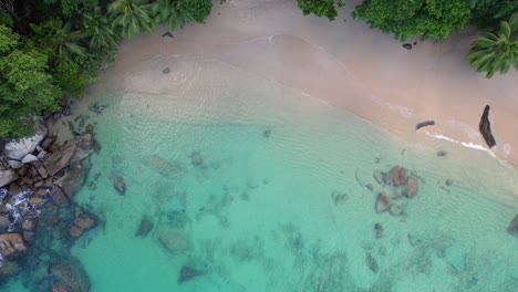 Drone-footage-of-white-sandy-beach,-coconut-palm-trees,-turquoise-water,-granite-stones-on-sunset-beach,-Mahe-Seychelles-30fps