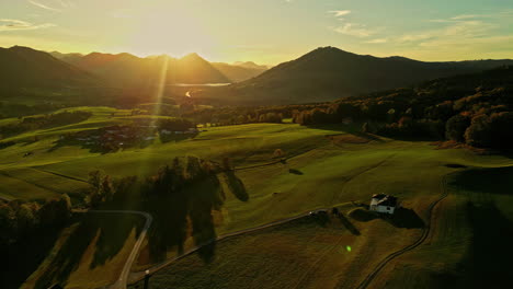 Sunrise-over-lush-green-meadows-in-a-village-in-Attersee,-Austria,-with-golden-light-spilling-over-rolling-hills-and-a-solitary-farmhouse