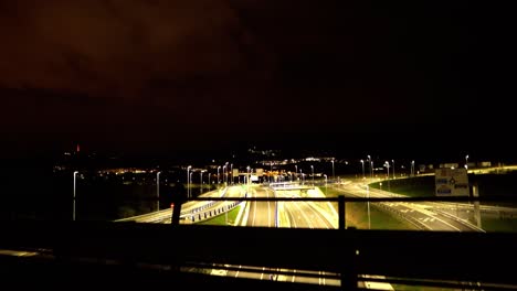 Cars-driving-by-on-lit-up-highway-at-night-aerial-freeway-bridge-view