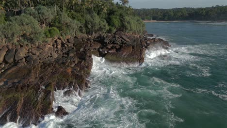 Long-Establishing-Aerial-Drone-Shot-Past-Rocky-Headland-to-Reveal-Hiriketiya-Beach-and-Bay-with-Surfers-in-the-Water-in-Southern-Sri-Lanka