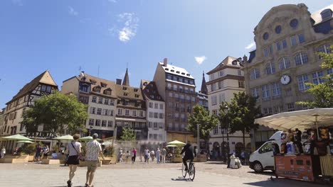 Gente-Caminando-Y-En-Bicicleta-En-La-Plaza-Del-Mercado-De-Estrasburgo,-Place-Kléber,-En-Un-Cálido-Día-De-Verano