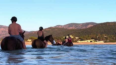 Los-Turistas-De-Vacaciones-Disfrutan-Montando-A-Caballo-En-El-Agua-De-Mar-En-La-Temporada-De-Verano-En-Córcega,-Francia.