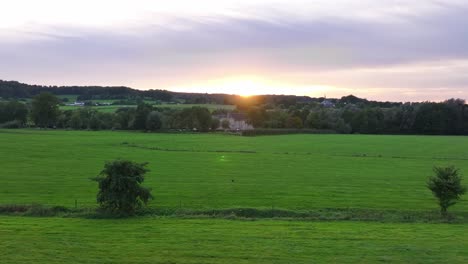 Sun-breaking-over-the-landscape-slope-in-distance,-lush-fields-foreground