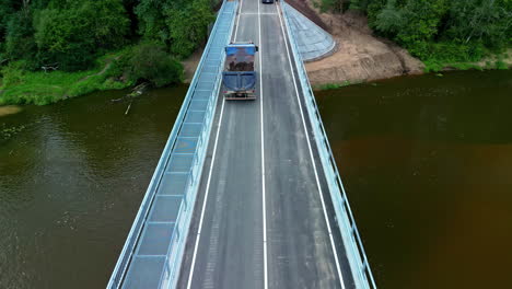 A-Reveal-Shot-Of-A-Dump-Truck-Driving-Across-The-Bridge-Approaching-A-Busy-Forest-Area