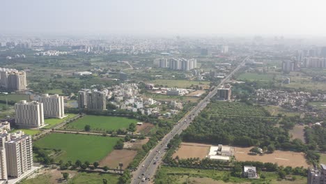 Vista-Aérea-De-La-Ciudad-De-Rajkot,-Un-Dron-Vuela-Sobre-La-Carretera-De-Kalavad,-Donde-Se-Ven-Muchos-Complejos-Y-Grillos-De-Caja-En-La-Carretera-Rodeada-De-Densos-árboles