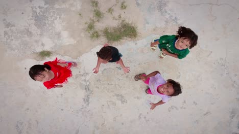 Southeast-Asian-children-jumping-happily-and-looking-up-at-camera,-top-angle-view