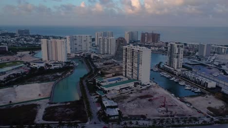 Drone-footage-of-Puerto-Cancun,-New-Mall-in-Cancun-Mexico,-a-luxury-residential-area-with-with-boats-in-a-marina,-wide-aerial-tilting-downward