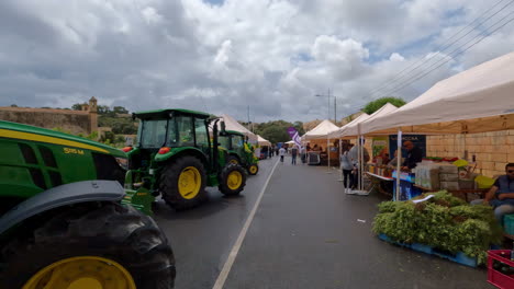 Mercado-De-Agricultores-Locales-En-Malta-Con-Tractores-Estacionados,-Vista-POV-Hacia-Adelante-Con-Plataforma-Rodante