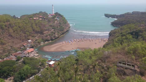 Aerial-view-of-bay-between-cliffy-shoreline-with-fishing-boats-harbor-and-lighthouse-on-the-top-of-cliff---Baron-beach,-Indonesia