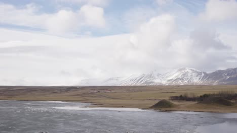 Bright-cloudy-day-with-wet-meadow-and-snowy-mountain-landscape,-Iceland