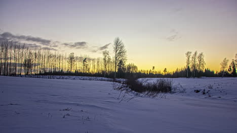 Wolken-Ziehen-In-Einem-Orange-gelben-Sonnenuntergang-über-Einer-Winterlandschaft-Vorbei