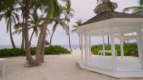 Classic-white-wedding-altar-next-to-a-paradisiacal-beach-with-palm-trees-and-the-sea