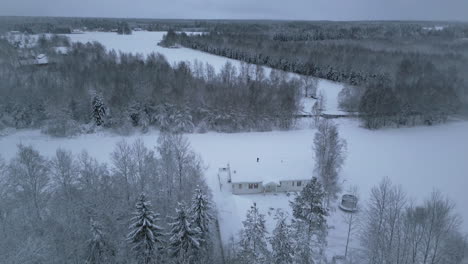 Nordisches-Haus-Mit-Schnee-Bedeckt,-Umgeben-Von-Wald,-Drohnenansicht-Aus-Der-Luft
