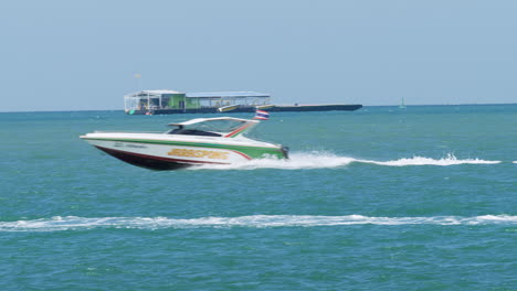 Una-Lancha-Veloz-Con-Una-Bandera-Nacional-Tailandesa-Que-Va-Hacia-La-Izquierda,-Revelando-Aguas-Rápidas-Y-Otros-Barcos-Al-Fondo,-Pattaya,-Tailandia