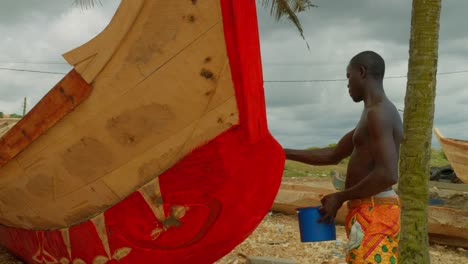 black-african-male-painting-a-wooden-boat-for-fishing-in-remote-village-in-ghana