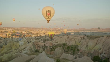 Globos-Aerostáticos-Vuelan-Sobre-El-Paisaje-Rocoso-De-La-Mañana-Besado-Por-El-Sol