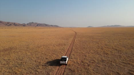 Der-Toyota-Hilux-Pickup-Fährt-Auf-Einer-Einzigen-Spur-über-Eine-Weite-Afrikanische-Ebene-Durch-Dreck-Und-Gras,-In-Der-Ferne-Liegen-Berge