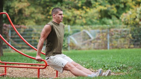 Muscular-athletic-man-doing-arm-push-ups-on-an-exercise-machine-in-a-park