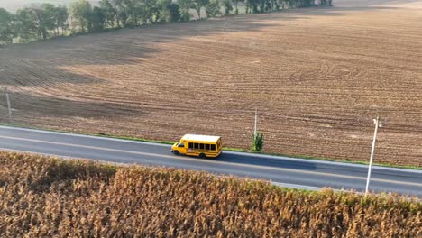 Aerial-tracking-shot-of-short-school-bus-driving-on-rural-road-in-USA
