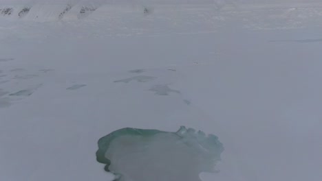 Vista-De-Drones-En-Svalbard-Volando-Sobre-Montañas-Blancas-Nevadas-Con-Un-Lago-Congelado-En-Noruega