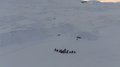 Drone-view-in-Svalbard-flying-over-snowy-white-mountains-with-a-line-of-snowmobiles-and-people-walking-in-Norway