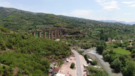 Drone-view-in-Albania-flying-over-a-green-landscape-with-a-road,-small-houses-and-a-big-column-bridge