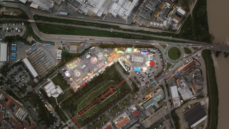Wide-top-down-aerial-timelapse-of-a-bright-carnival-in-the-town-of-Alba,-Italy-with-lots-of-traffic-moving-around-it-on-the-roads