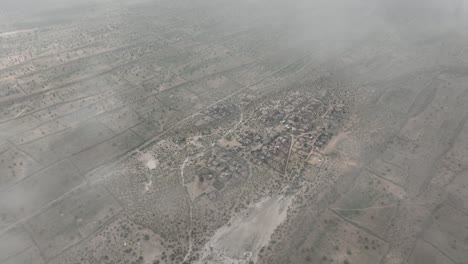 Aerial-drone-shot-flying-high-over-desert-life-in-a-tiny-village-in-Tharparkar,-Sindh,-Pakistan-on-a-cloudy-day