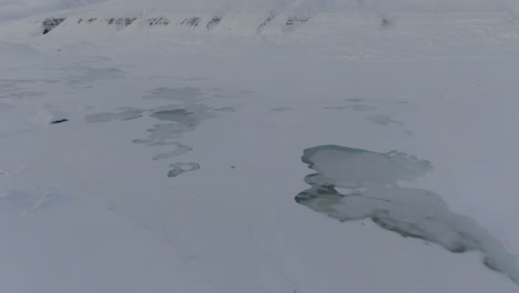 Drohnenansicht-In-Spitzbergen,-Die-An-Einem-Bewölkten-Tag-über-Schneeweiße-Berge-Mit-Zugefrorenen-Seen-In-Norwegen-Fliegt