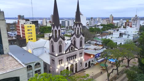 Rotating-aerial-of-the-San-Jose-Cathedral-frontal-view,-street-with-pedestrians-walking-and-cityscape-background