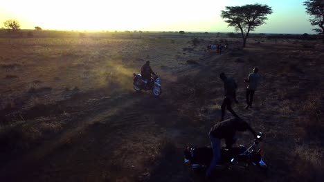 African-Men-Dancing-And-Riding-Motorcycles-On-Dusty-Terrain-At-Sunset-In-Uganda