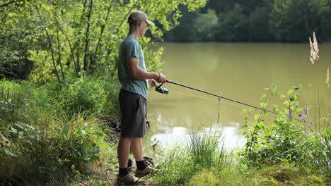 Young-male-angler-turns-the-winch-of-fishing-rod-and-reels-in-the-line-on-cloudy-murky-lake