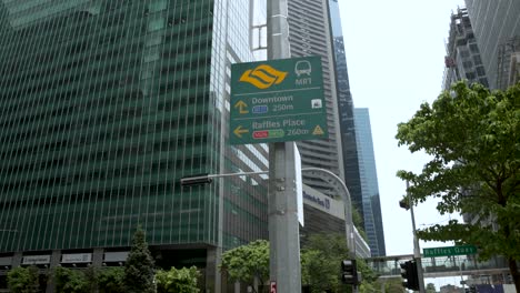 Looking-Up-At-Road-Sign-With-Tilt-Down-To-Reveal-Lunchtime-Office-Workers-Waiting-At-Pedestrian-Crossing-On-Raffles-Quay-In-Downtown-Singapore-In-September