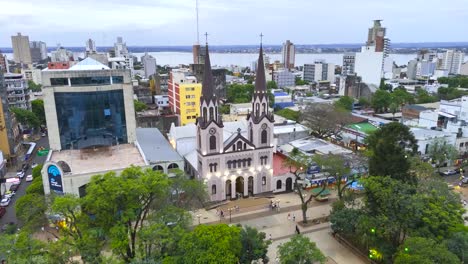 Rotating-aerial-view-of-the-San-Jose-cathedral-in-Posadas,-Argentina,-cityscape-and-the-Paraná-River-background