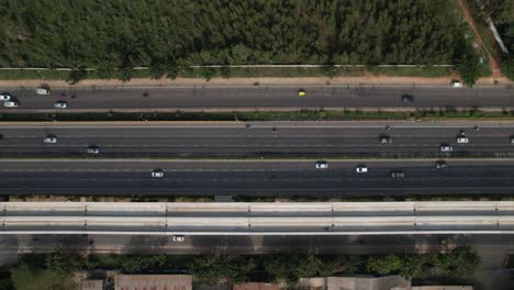 Indian-Motorway-in-a-cinematic-aerial-view-showing-fast-moving-vehicles-and-metro-railway-bridge-construction-above-the-service-road