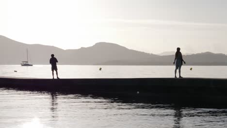 Ruhige-Silhouetten-Umarmen-Den-Sonnenaufgang-Am-Pier,-Während-Sie-Meditieren-Und-Sich-In-Der-Wärme-Der-Sonne-Sonnen