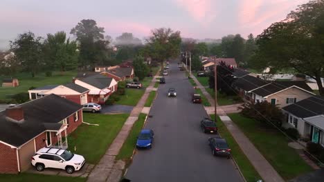 Car-driving-through-quaint-American-neighborhood-during-foggy-morning-sunrise