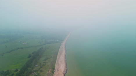 An-Aerial-Shot-Of-A-Misty-Green-Coastal-Landscape-With-Forests-And-The-Waves-On-The-Shoreline