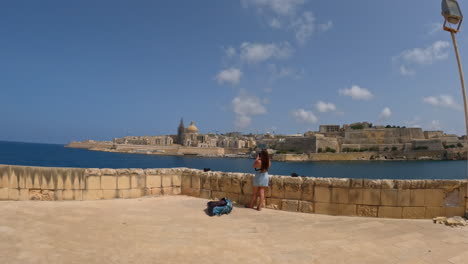 A-lady-stands-on-a-wall-overlooking-the-peninsula-with-the-city-of-Valletta-in-Malta
